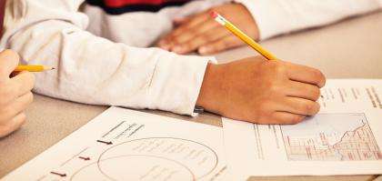 Student's hand holding a pencil, writing on worksheets featuring a Venn diagram and a map.