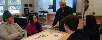 A teacher gathered around a table with four students, having a discussion on an educational resource. 