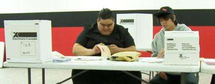 In a polling station, two poll workers are seated at a table with election materials.