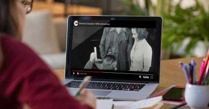 Young student studying from home with Elections Canada’s 100th anniversary Web content open on a laptop.