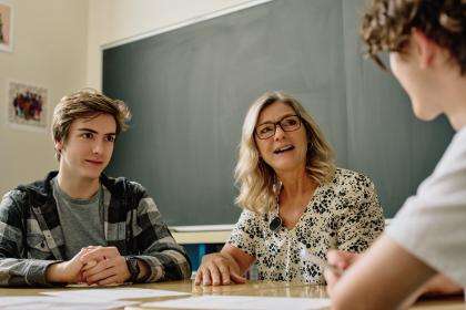 In a classroom, a group of students and a teacher are talking.