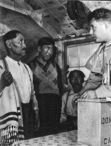 Black and white photo taken in Labrador (Nunatsiavut) during an election. Returning officer Harry Nosworthy swears in Joe Millik as an election official.