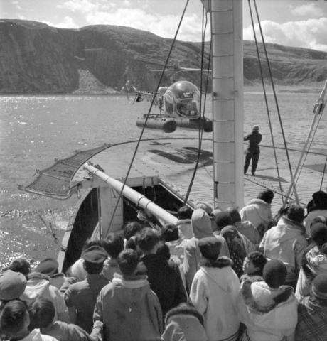 Black and white photo of a group of Inuit watching a helicopter taking off in Salluit, Nunavik, Quebec. 