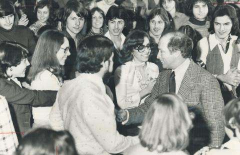CE08-Youth-L Black and white photograph of Prime Minister Pierre Trudeau shaking hands with a young person, while standing at the centre of a large group of smiling youth.