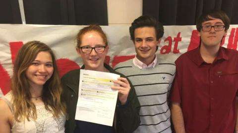 Photograph of four smiling teenagers holding up a piece of paper.  