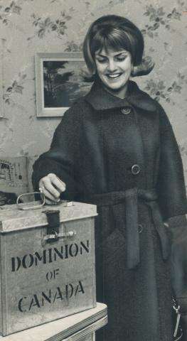 Black and white photograph of a young women placing her ballot in a metal ballot box, while smiling.