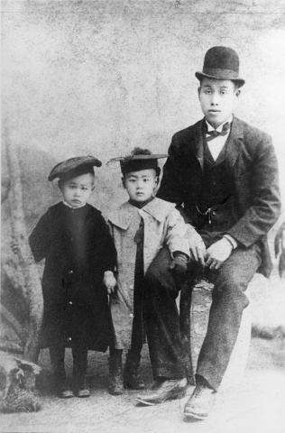 A black and white photograph of a Japanese man seated beside his two young children.