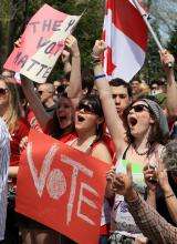 00-Context-card-Youth A photograph showing a group of young people protesting, waving Canadian flags and signs that say “vote.”