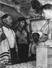 VRTT_Inuit_1953_EN Black and white photo taken in Labrador (Nunatsiavut) during an election. Returning officer Harry Nosworthy swears in Joe Millik as an election official.