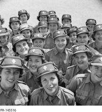 CE06-Youth Black and white photograph showing a large group of women wearing military uniforms smiling at the camera.