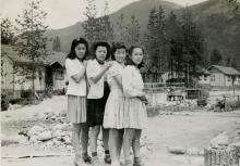 Japanese Canadians Context Card Black and white photograph of four young Japanese women standing in front of an internment camp, with their hands on one another's shoulders. Mountains are in the background.