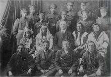 VRTT_FNP_1917_EN Black and white photo of the first time Indigenous men joined the Canadian Forces as soldiers. First two rows: Indigenous men, some in traditional regalia. Last two rows: men in their soldier uniform.