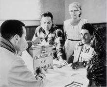 VRTT_FNP_1962_EN Black and white photo in Hiawatha Council Hall on the occasion of a federal by-election. The first votes cast since the right to vote was extended to all status Indians were those of the Rice Lake Band near Peterborough, Ontario. From left to right: Lawrence Salleby; Chief Ralph Loucks, Deputy Returning Officer; Lucy Muskrat, Poll Clerk; Eldon Muskrat, Poll Constable.